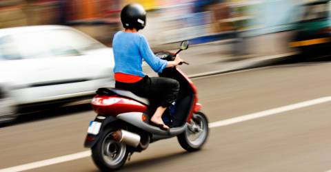 Vrouw met scooter rijdt snel over de weg